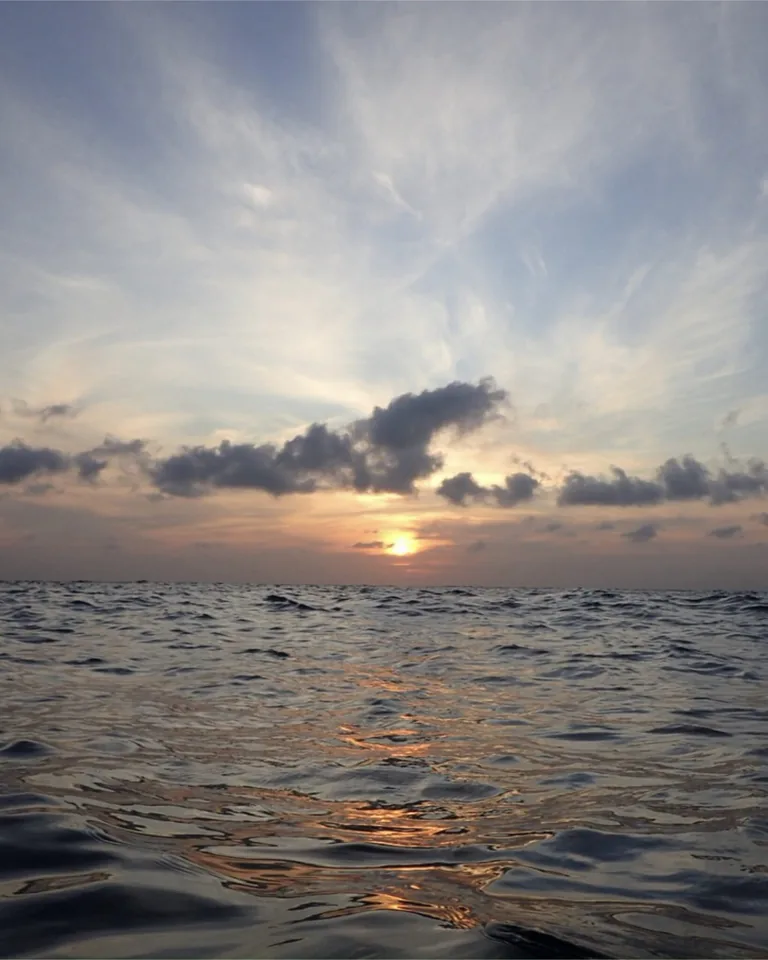 Sunset over the ocean off Bali seen from water level, the sun glowing below a band of dark clouds