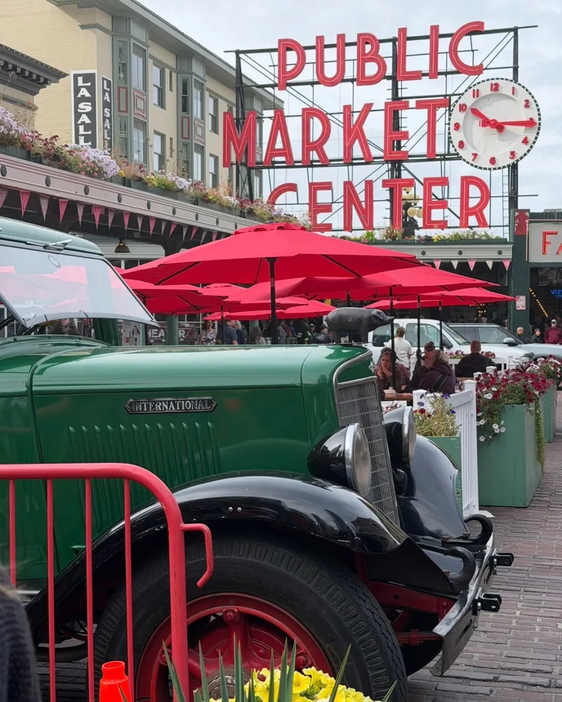 Vintage green International truck parked beneath the neon Public Market Center sign and clock at Pike Place Market, Seattle